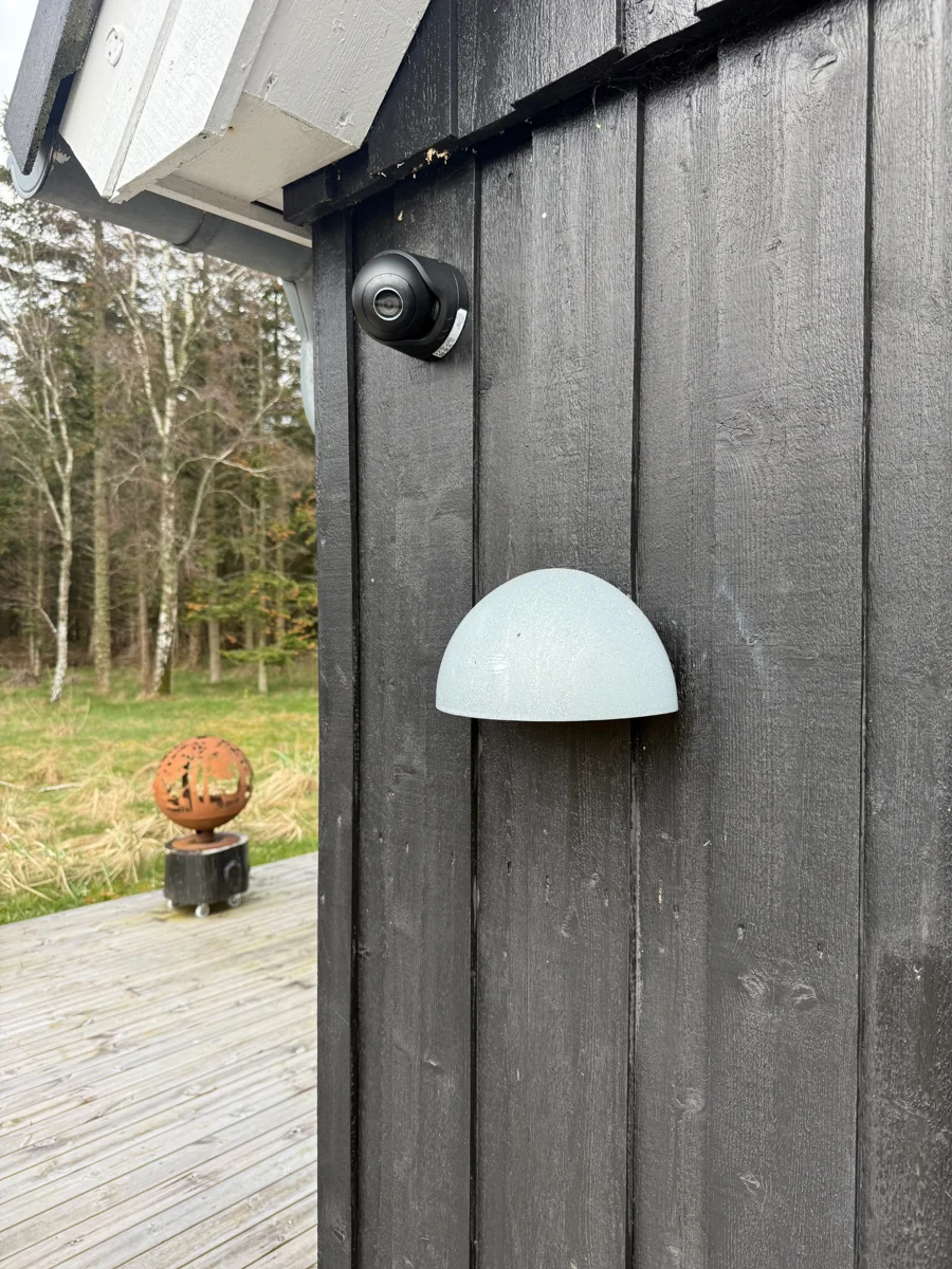 Sort kamera på en mørk træfacade over en udendørslampe